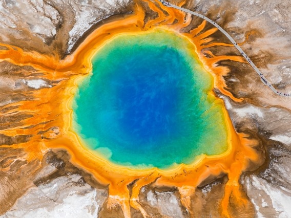 aerial view of Grand Prismatic Spring in Yellowstone National Park, a geyser pool that is deep blue and green in the center and orange and red on the edges, surrounded by arid landscape
