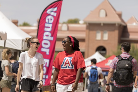 Two students walking at an event on the University of Arizona Mall